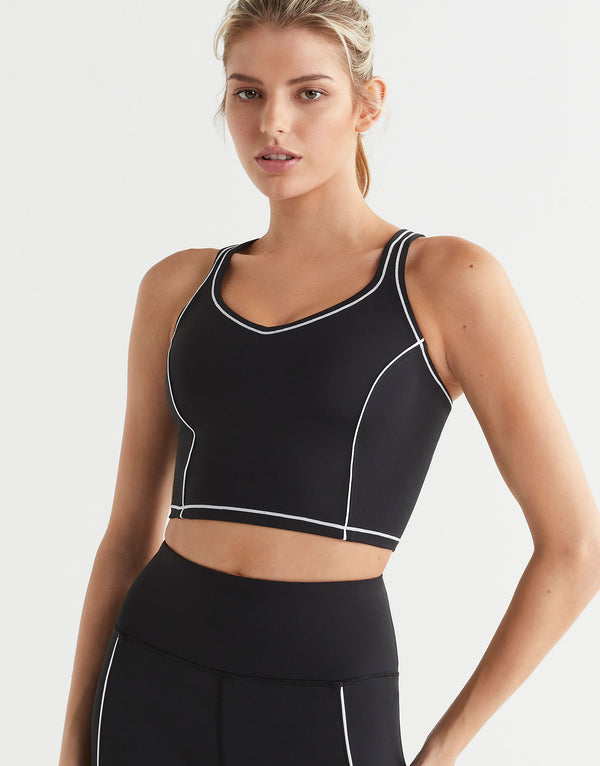 Woman wearing a black sports bra with white accents on a light gray background