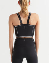 Person wearing a black sports bra and leggings with white accents on a light gray background