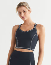 Woman wearing a black sports bra with white accents on a light gray background