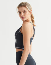 Woman wearing a black sports bra with white accents on a light gray background