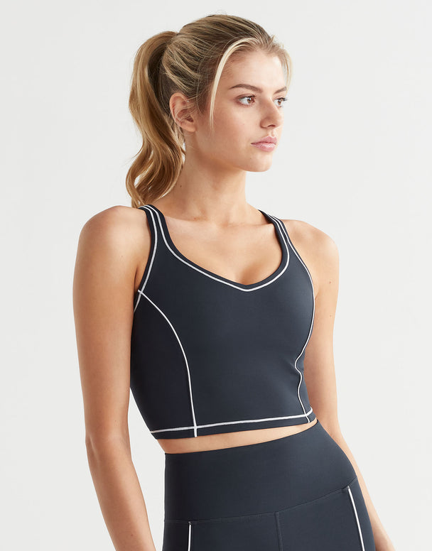 Woman wearing a black sports bra with white piping on a light gray background