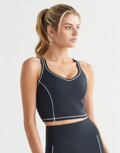 Woman wearing a black sports bra with white piping on a light gray background