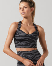 Woman wearing a black camouflage sports bra and leggings on a light gray background