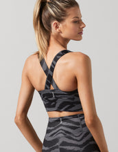 Woman wearing a black and gray patterned sports bra and leggings on a light gray background