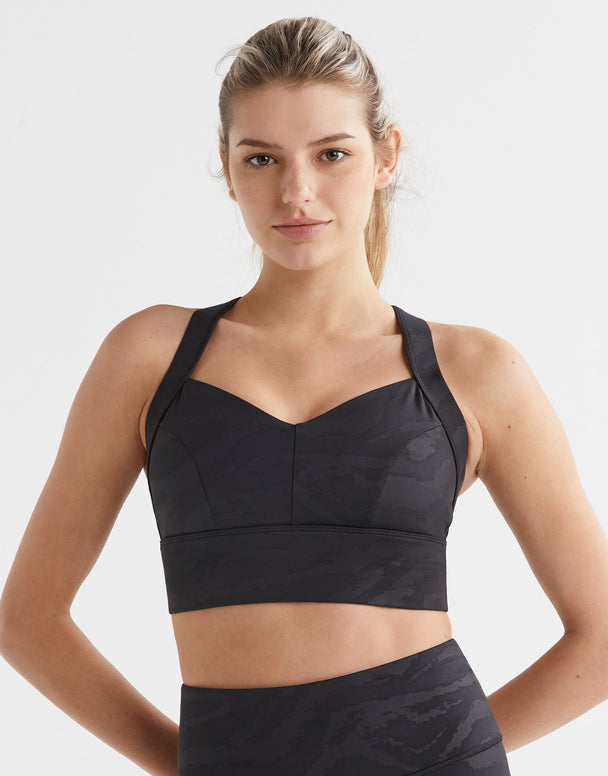 Woman wearing a black sports bra and leggings on a light gray background