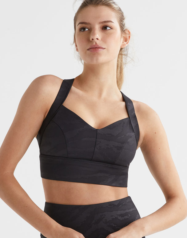 Woman wearing a black sports bra and leggings on a light gray background