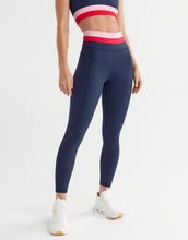 Person wearing navy leggings with a white and red crop top on a light gray background
