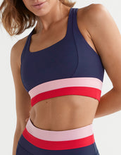 Navy, pink, and red sports bra on a model against a white background