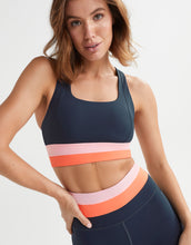 Woman wearing a sports bra and leggings with a striped design on a plain background