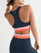 Navy sports bra with pink and orange stripes worn by a person on a light gray background