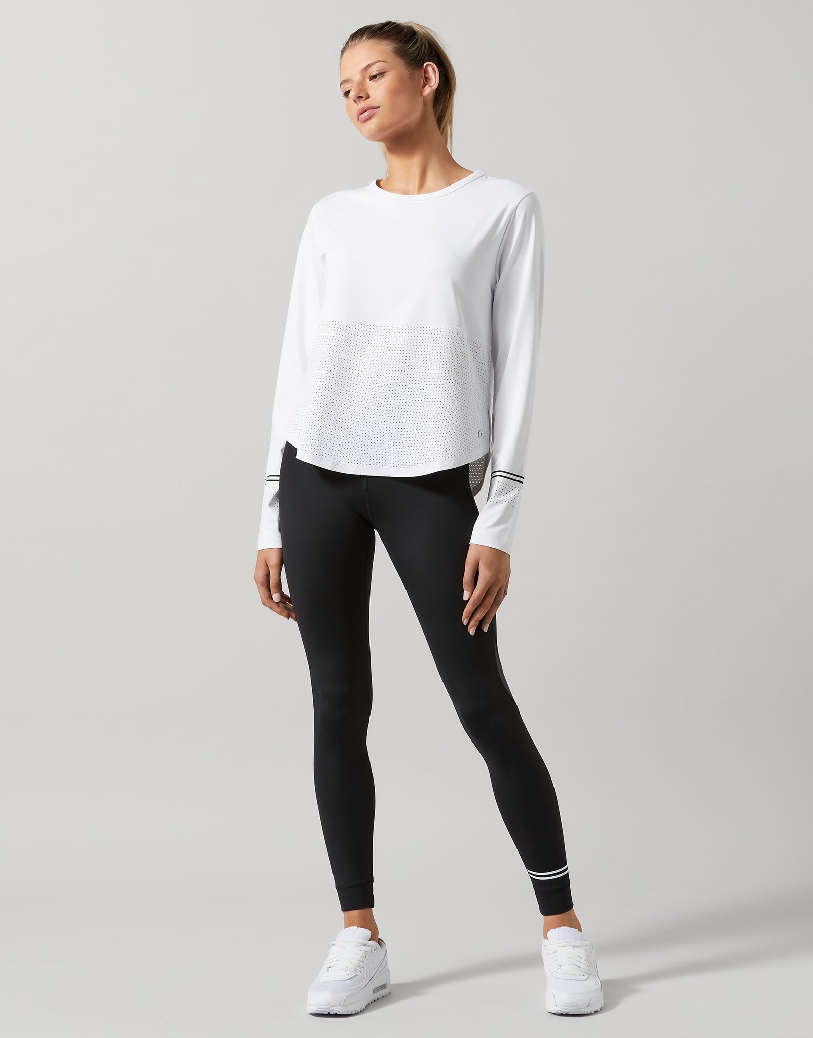Woman wearing a white long-sleeve top and black leggings on a gray background