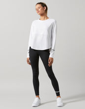 Woman wearing a white long-sleeve top and black leggings on a gray background