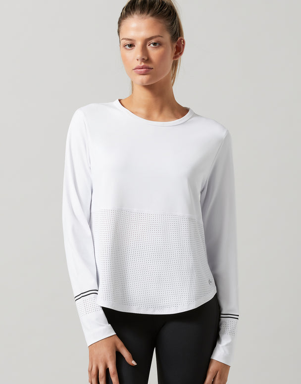 Woman wearing a white long-sleeve athletic top with black leggings on a gray background