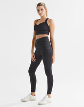 Woman wearing a black sports bra and leggings set on a white background
