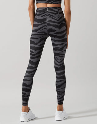 A model shown from the back wearing high-waisted leggings with a dark gray and black zebra stripe pattern, paired with white sneakers, against a light gray studio background.