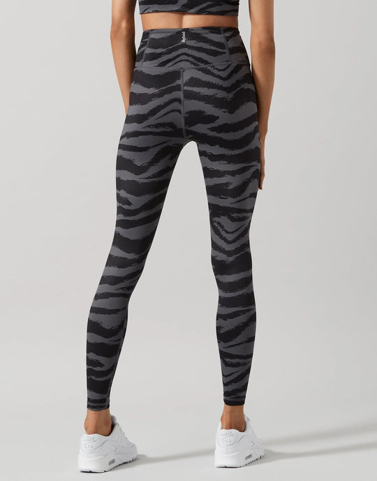 A model shown from the back wearing high-waisted leggings with a dark gray and black zebra stripe pattern, paired with white sneakers, against a light gray studio background.