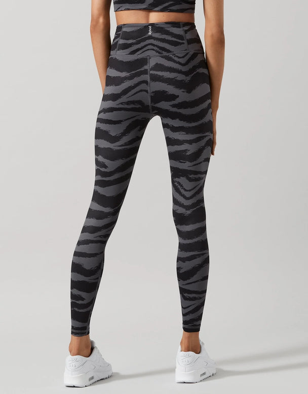 A model shown from the back wearing high-waisted leggings with a dark gray and black zebra stripe pattern, paired with white sneakers, against a light gray studio background.