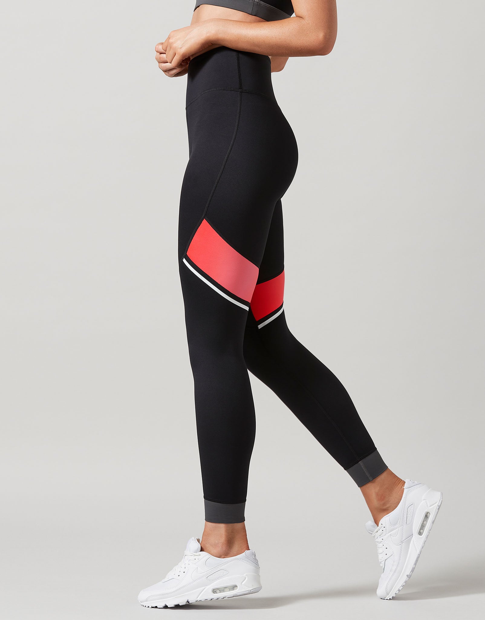 A model wearing black leggings with pink and grey accents on a grey background.