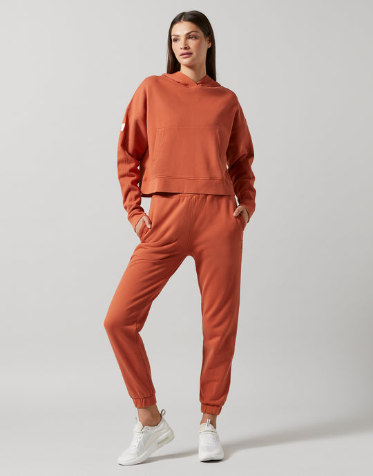 A woman wearing a copper hooded sweater and sweatpants and white shoes.