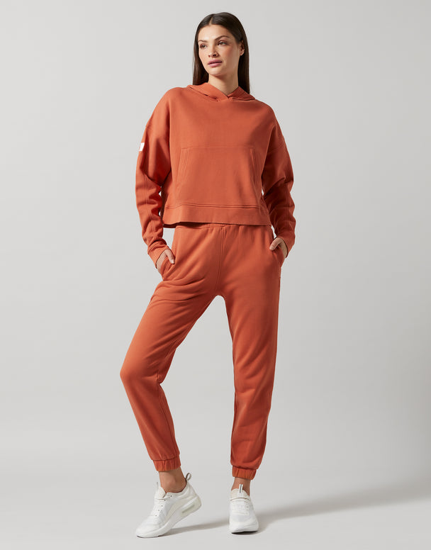 A woman wearing a copper hooded sweater and sweatpants and white shoes.