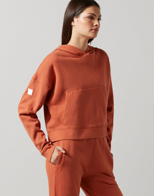 A woman wearing a copper wash hoodie sweater with an oversized fit and a front kangaroo pocket, paired with matching lounge pants.