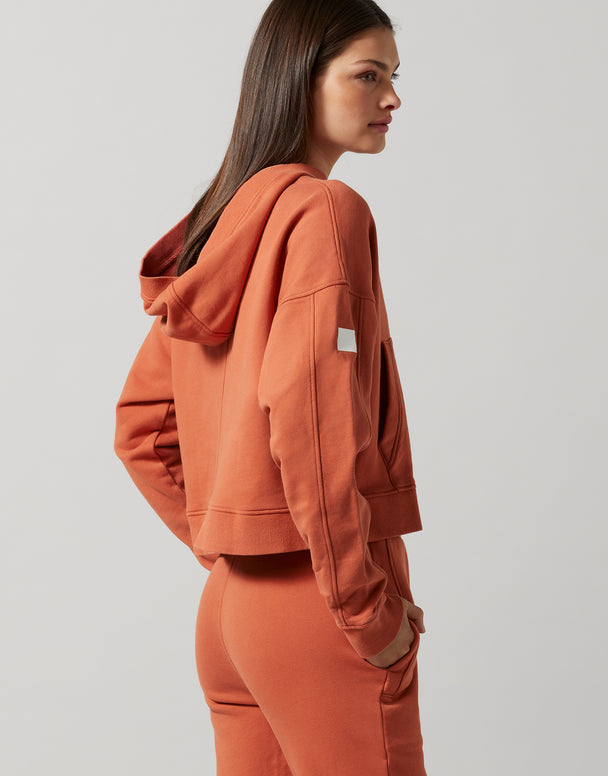 A woman wearing a copper hooded sweater with a logo and sweatpants.