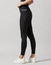 A model in a pair of high-waisted, full-length leggings in smoke black color, featuring breathable mesh panels and two pockets at the hip.