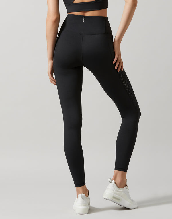 A woman wearing a pair of high-waisted, full-length leggings in smoke black color, featuring breathable mesh panels and two pockets at the hip.