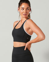 Woman wearing a black sports bra and leggings on a light gray background