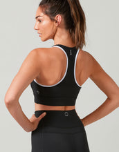 Woman wearing a black sports bra and leggings on a light gray background