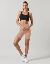 Woman wearing a black sports bra and pink shorts on a plain background