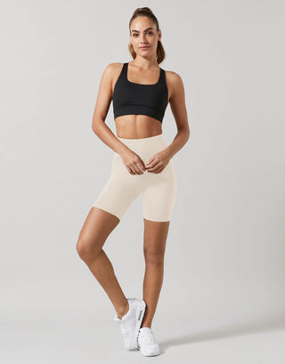 Woman wearing a black sports bra and beige shorts on a plain background
