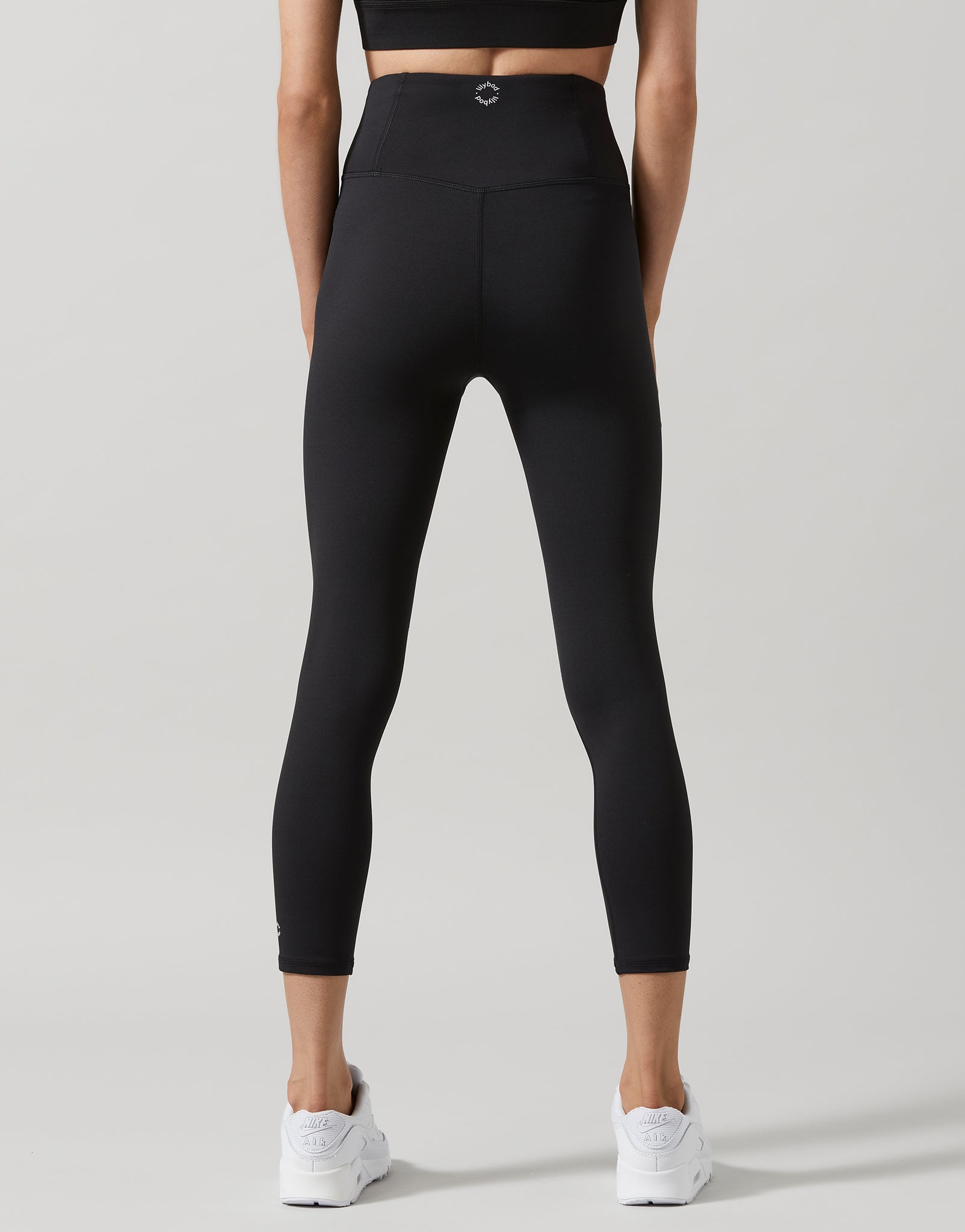 A woman wearing black 7/8 length leggings and white runners.