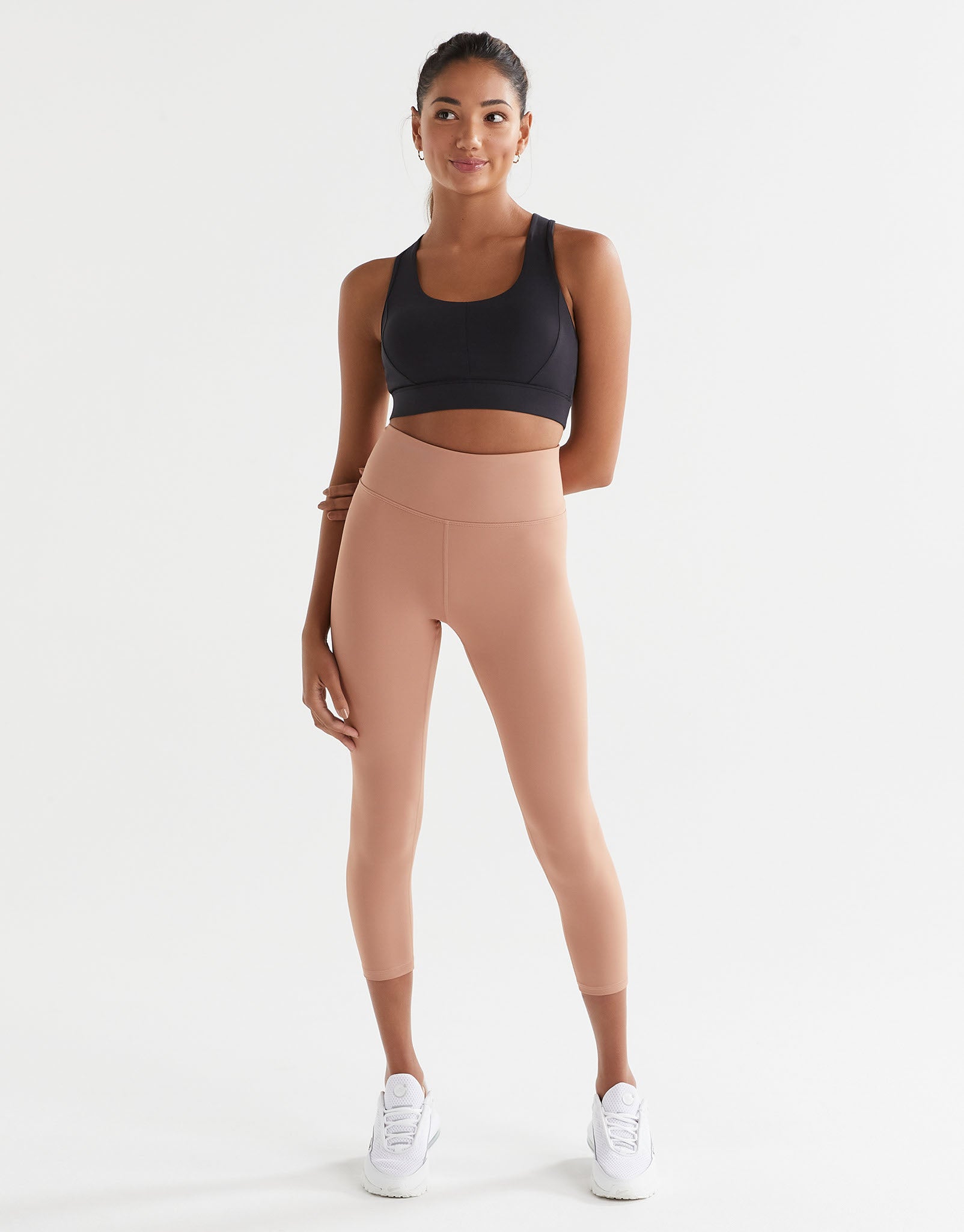 Woman wearing a black sports bra and beige leggings on a white background
