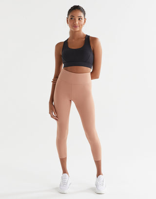 Woman wearing a black sports bra and beige leggings on a white background