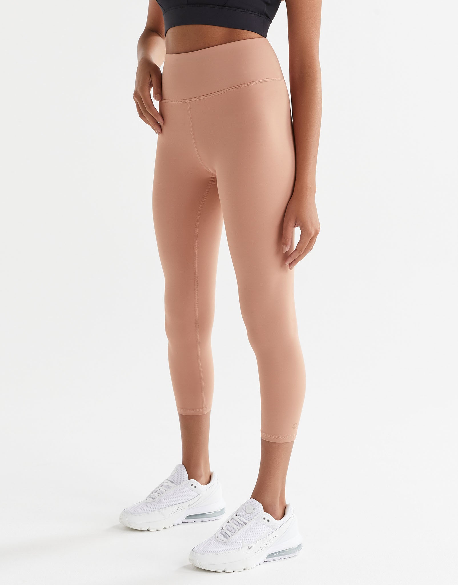 Person wearing beige leggings and white sneakers on a white background