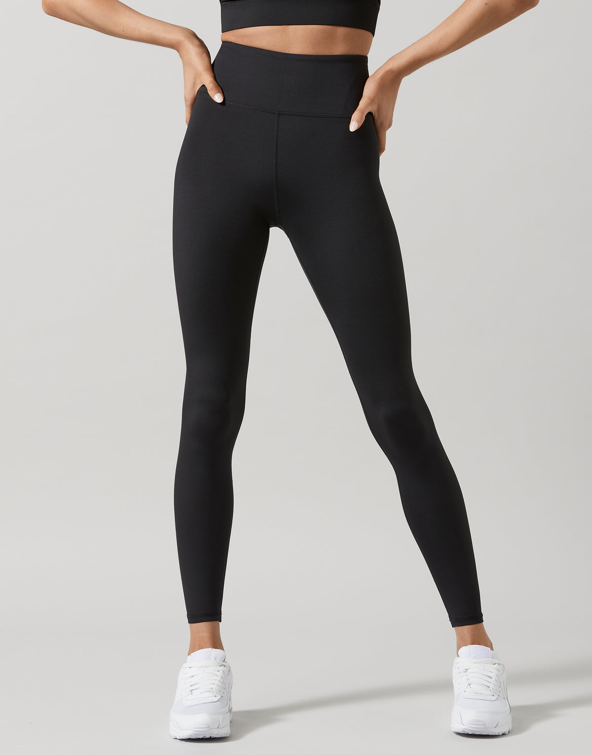A model wearing black high-waisted full-length leggings, standing with one hand on her hip.
