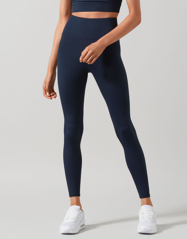 A person wearing high-waisted full-length blue leggings and white sneakers.