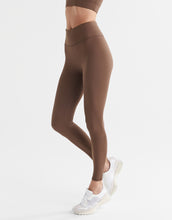 A woman wearing a pair of full-length brown leggings with a high-waisted fit, paired with a matching sports bra and white sneakers.