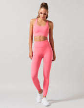 Woman wearing a pink sports bra and leggings set on a light gray background