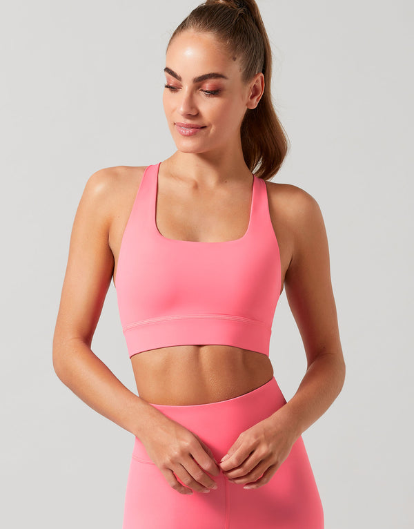 Woman wearing a pink sports bra and leggings on a light gray background