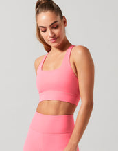 Woman wearing a pink sports bra and leggings on a gray background