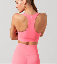 Woman wearing a pink sports bra and leggings on a light gray background