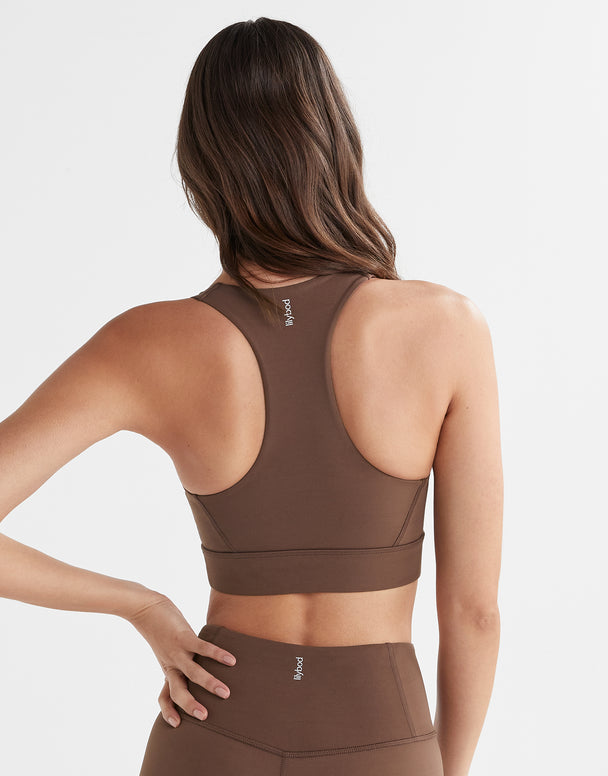 A model wearing a brown Lilybod Astrid sports bra with a scoop front neckline and wider straps.