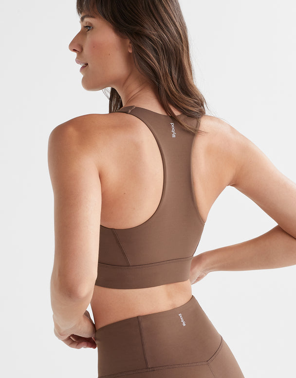 Woman wearing a brown sports bra and leggings on a light gray background