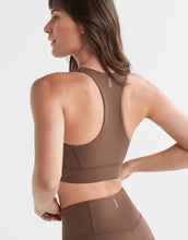 Woman wearing a brown sports bra and leggings on a light gray background