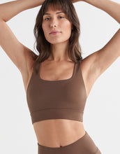 Woman wearing a brown sports bra and leggings on a white background