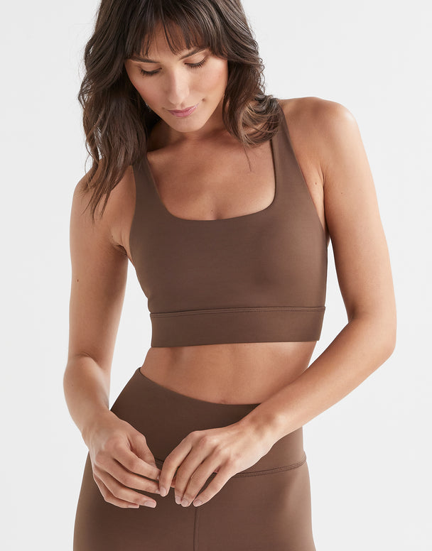 A woman wearing a brown Lilybod Astrid sports bra with a scoop front neckline and wider straps.