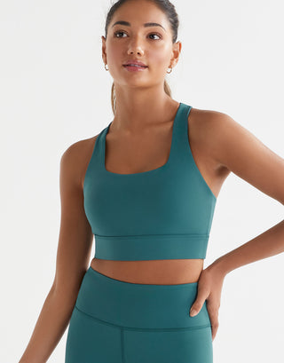 A woman wearing a teal Lilybod Astrid Ultra Core Sports Bra with a scoop front neckline and wider straps and Zahlee leggings.