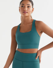 Woman wearing a teal sports bra and leggings on a white background